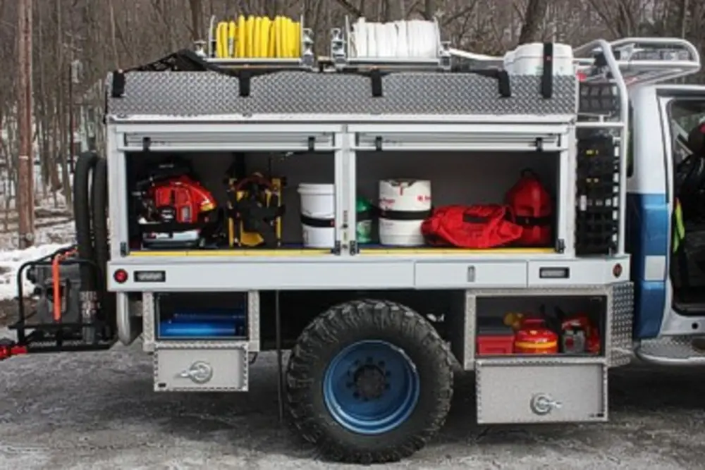 Exterior view of small fire truck showing cab, body compartments, and wheel/tire area.