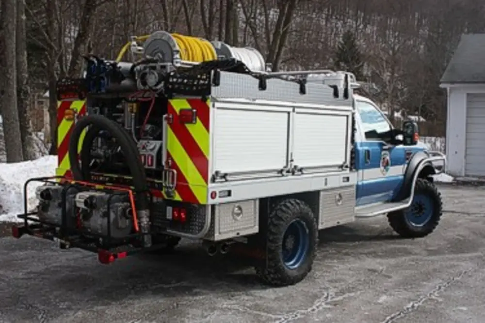 Exterior view of small fire truck showing cab, body compartments, and wheel/tire area.