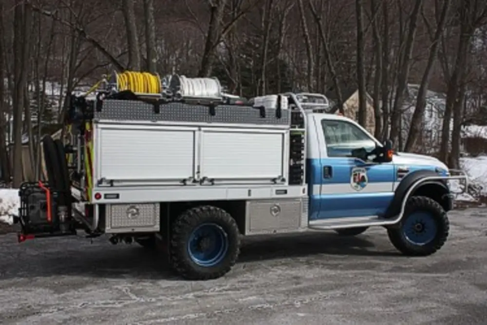 Exterior view of small fire truck showing cab, body compartments, and wheel/tire area.