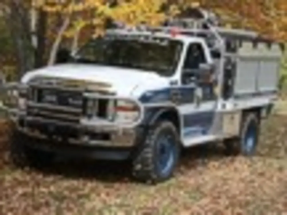 Exterior view of small fire truck showing cab, body compartments, and wheel/tire area.