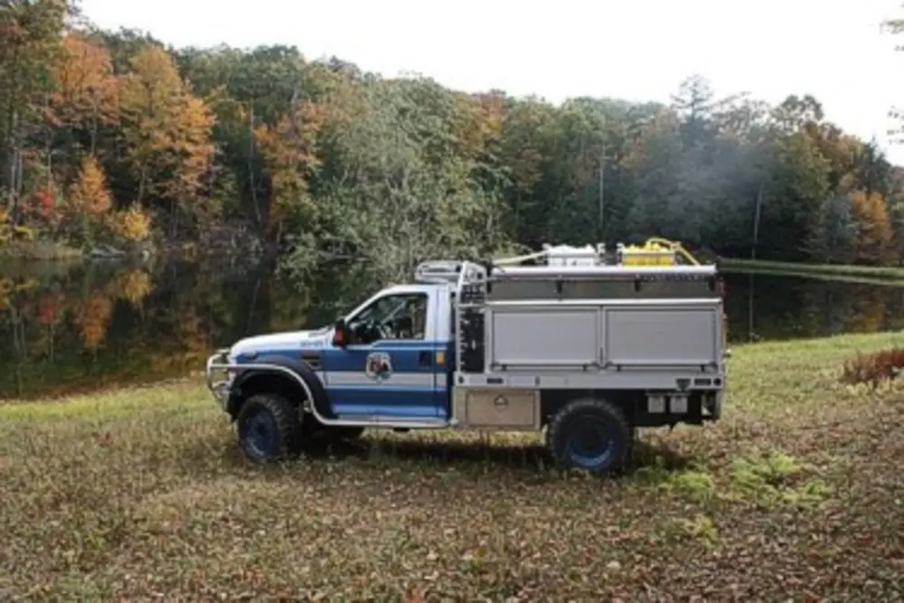 Exterior view of small fire truck showing cab, body compartments, and wheel/tire area.
