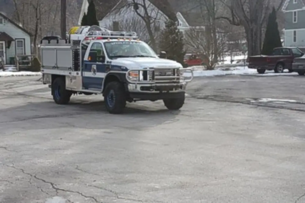 Exterior view of small fire truck showing cab, body compartments, and wheel/tire area.