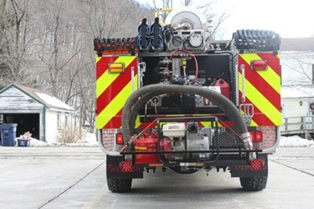 Exterior view of small fire truck showing cab, body compartments, and wheel/tire area.