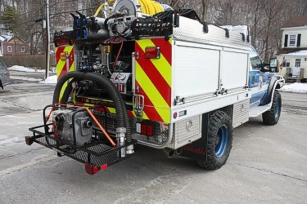 Exterior view of small fire truck showing cab, body compartments, and wheel/tire area.