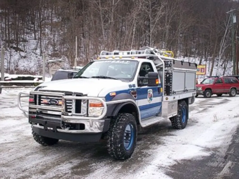 Exterior view of small fire truck showing cab, body compartments, and wheel/tire area.