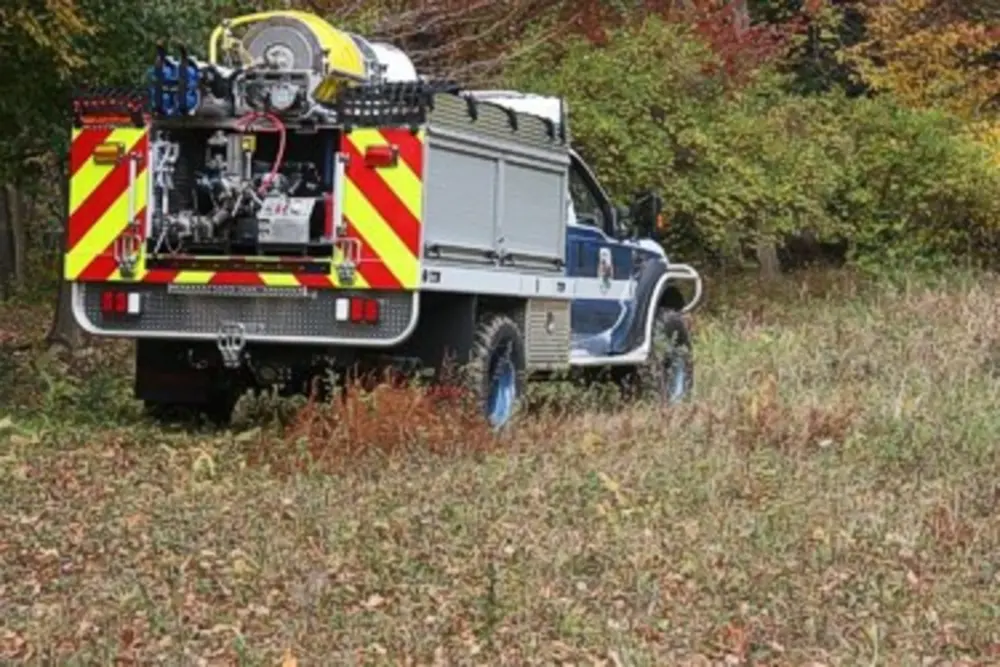 Exterior view of small fire truck showing cab, body compartments, and wheel/tire area.