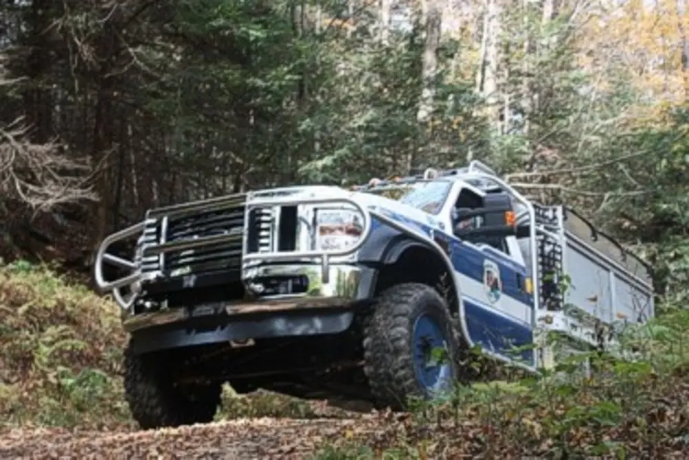 Exterior view of small fire truck showing cab, body compartments, and wheel/tire area.