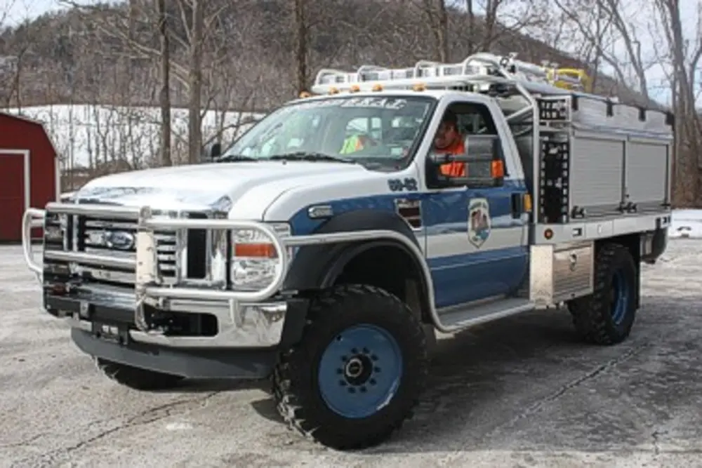 Exterior view of small fire truck showing cab, body compartments, and wheel/tire area.