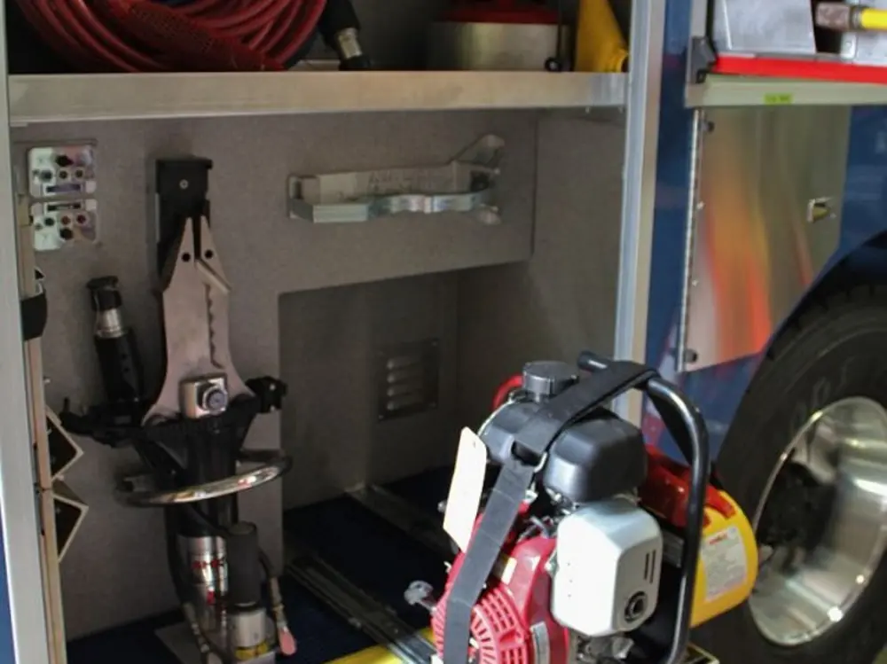 Exterior view of small fire truck showing cab, body compartments, and wheel/tire area.