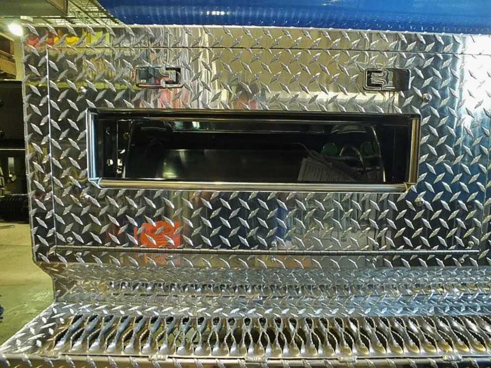 Exterior view of small fire truck showing cab, body compartments, and wheel/tire area.
