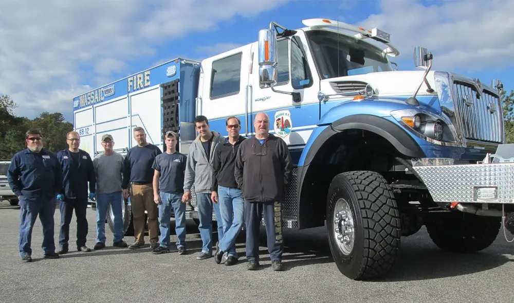 Exterior view of small fire truck showing cab, body compartments, and wheel/tire area.