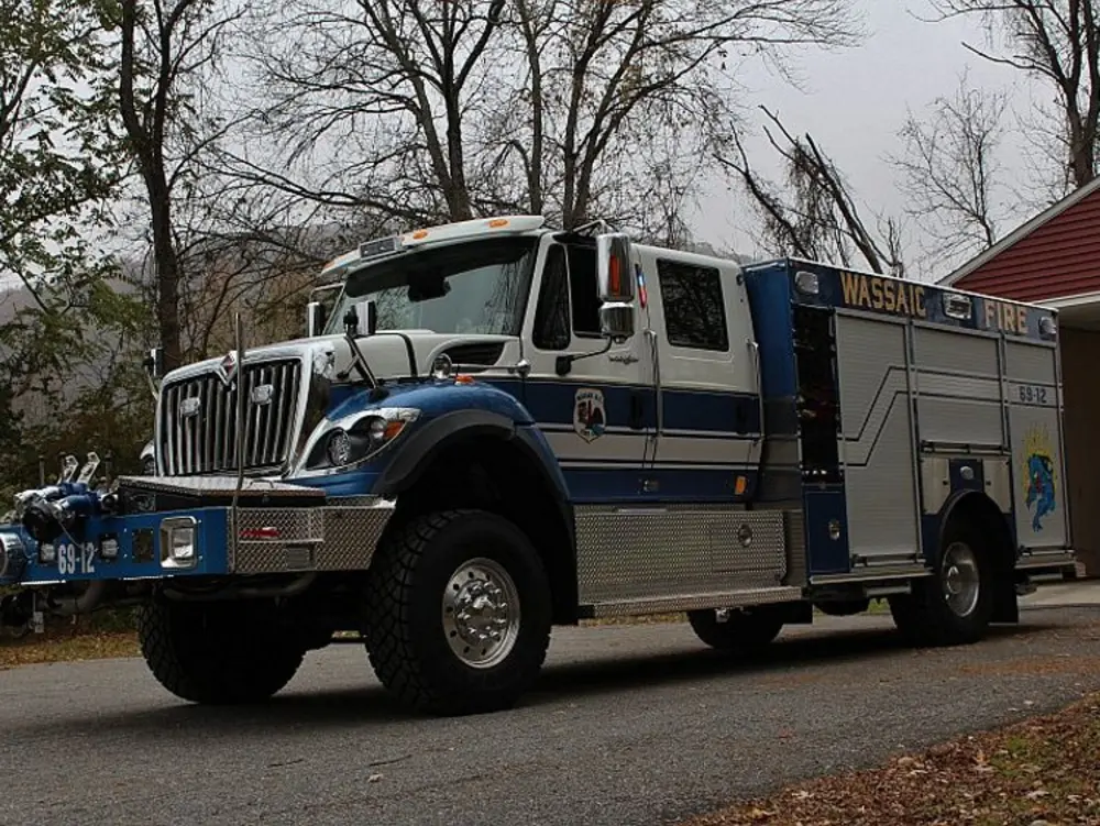 Exterior view of small fire truck showing cab, body compartments, and wheel/tire area.