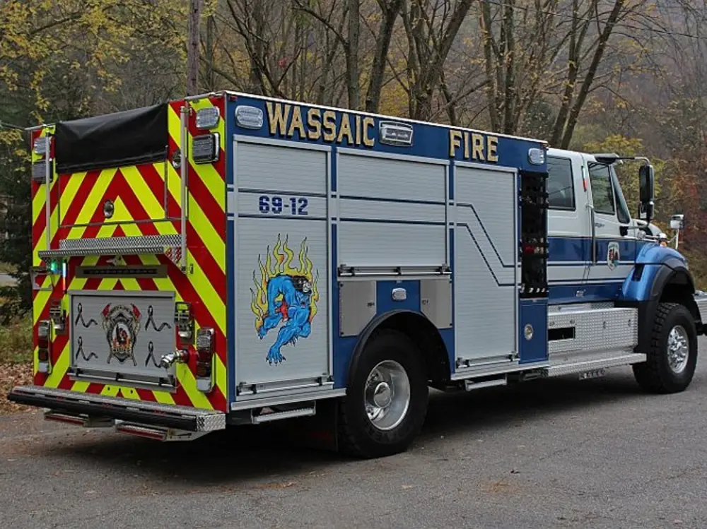 Exterior view of small fire truck showing cab, body compartments, and wheel/tire area.