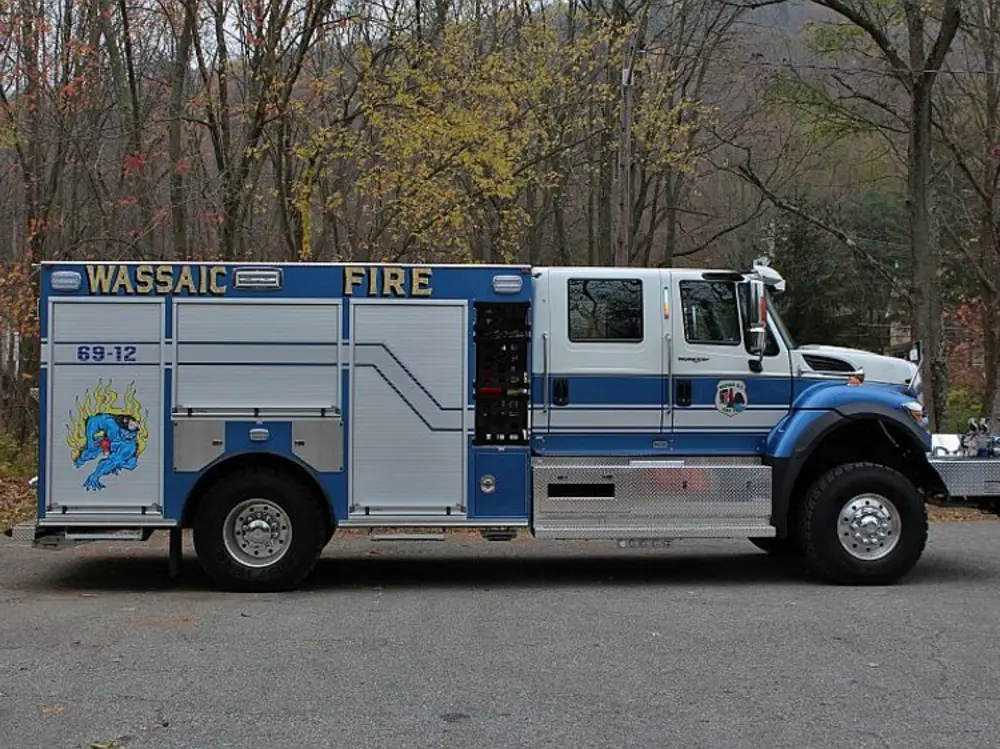 Exterior view of small fire truck showing cab, body compartments, and wheel/tire area.