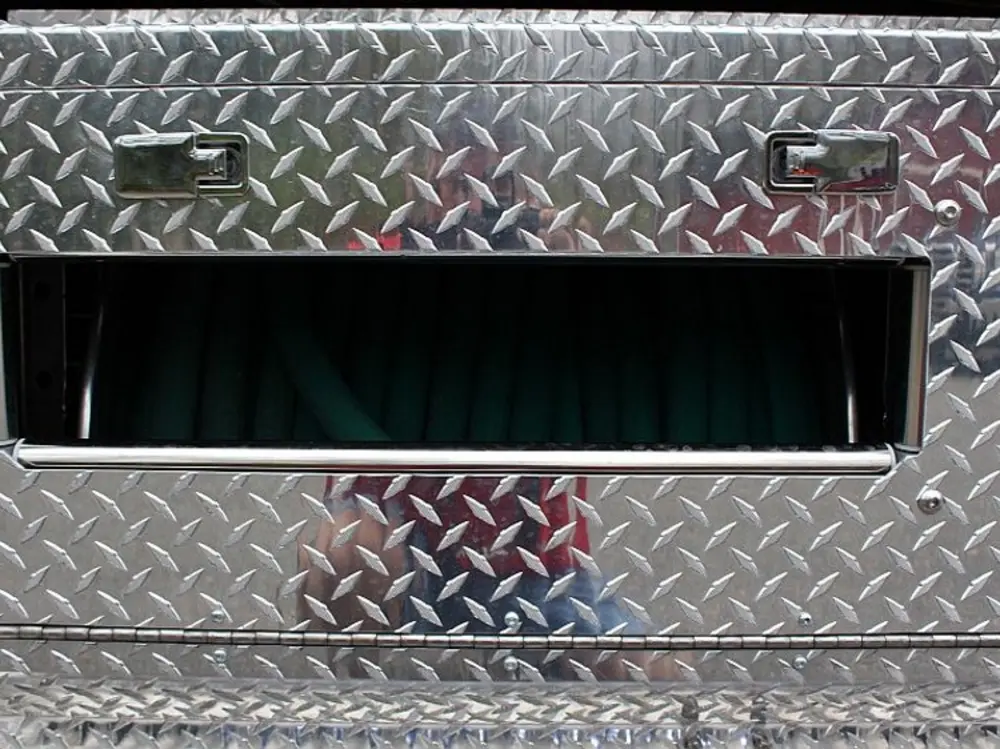Exterior view of small fire truck showing cab, body compartments, and wheel/tire area.