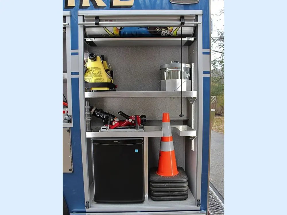 Exterior view of small fire truck showing cab, body compartments, and wheel/tire area.
