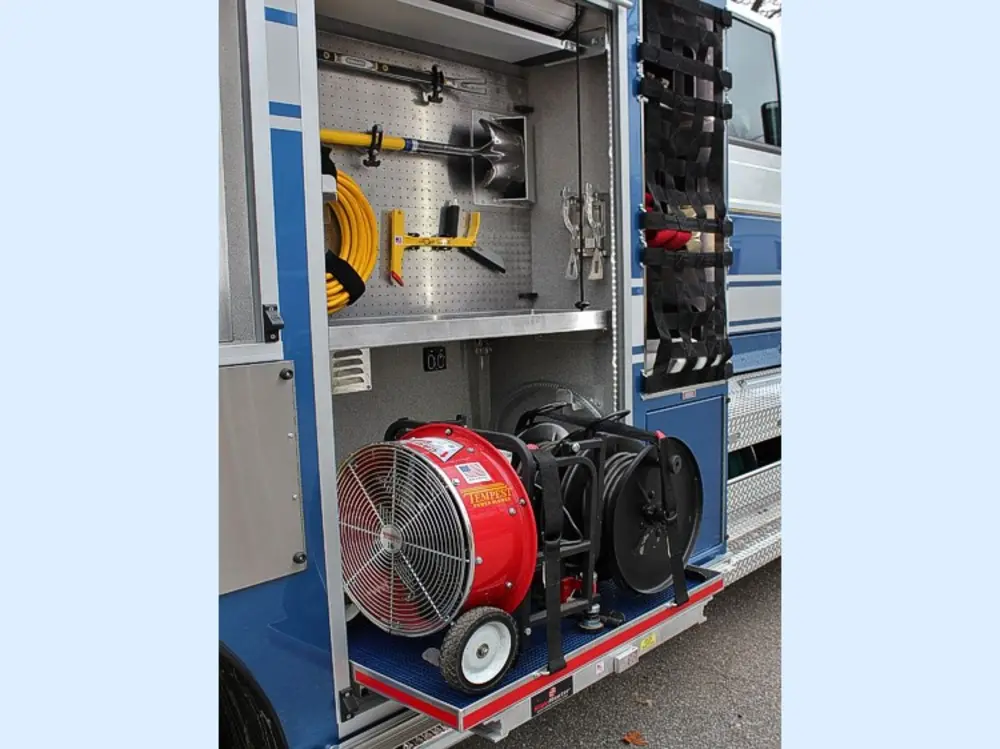 Exterior view of small fire truck showing cab, body compartments, and wheel/tire area.