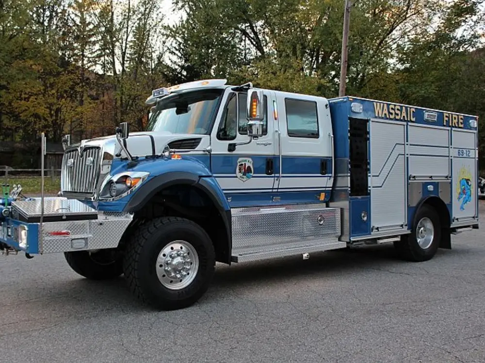 Exterior view of small fire truck showing cab, body compartments, and wheel/tire area.