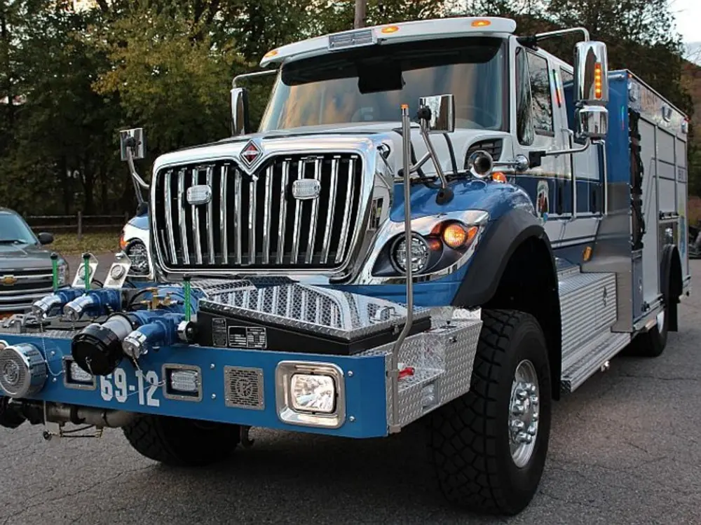 Exterior view of small fire truck showing cab, body compartments, and wheel/tire area.