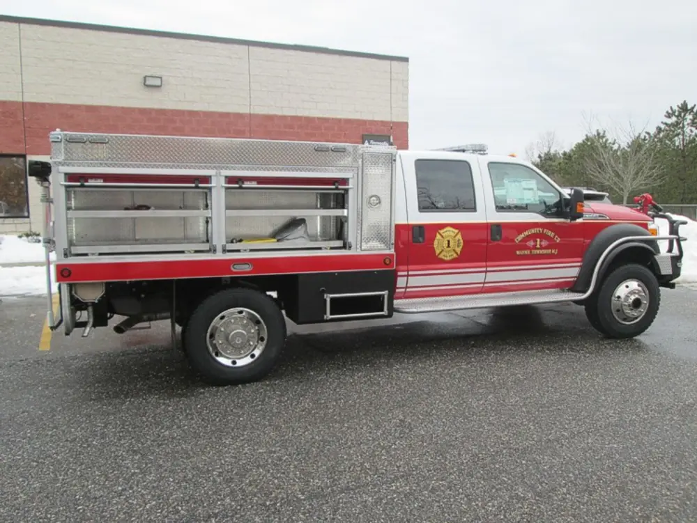 Exterior view of small fire truck showing cab, body compartments, and wheel/tire area.
