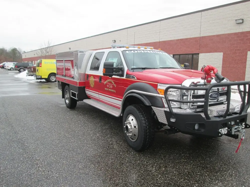 Exterior view of small fire truck showing cab, body compartments, and wheel/tire area.