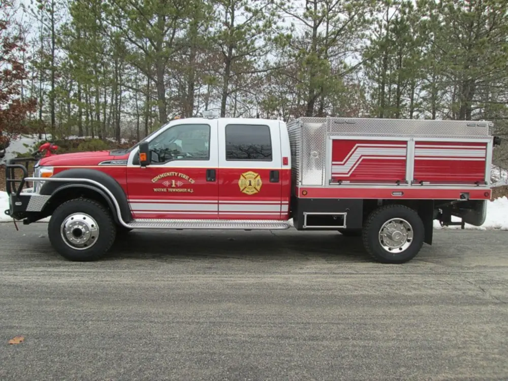 Exterior view of small fire truck showing cab, body compartments, and wheel/tire area.