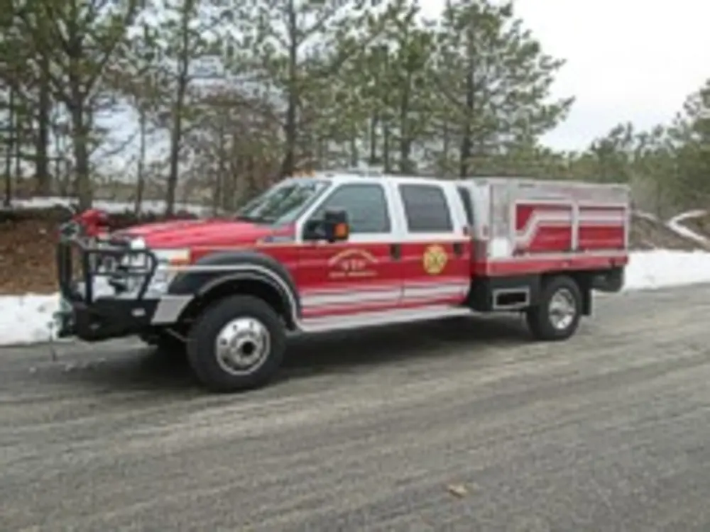 Exterior view of small fire truck showing cab, body compartments, and wheel/tire area.