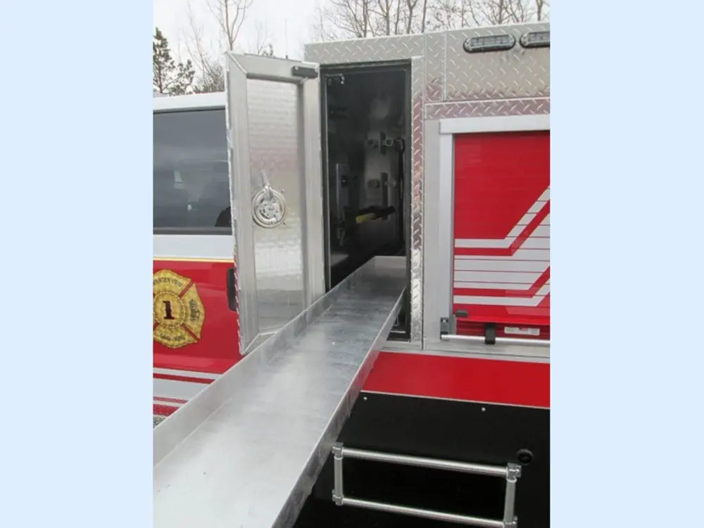 Exterior view of small fire truck showing cab, body compartments, and wheel/tire area.
