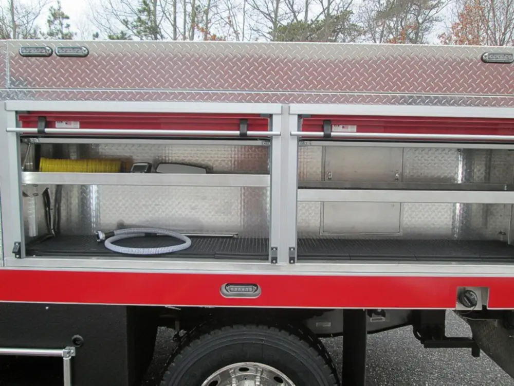 Exterior view of small fire truck showing cab, body compartments, and wheel/tire area.