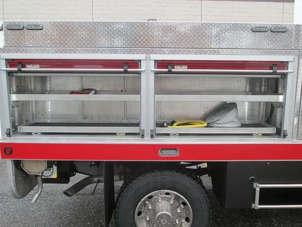 Exterior view of small fire truck showing cab, body compartments, and wheel/tire area.
