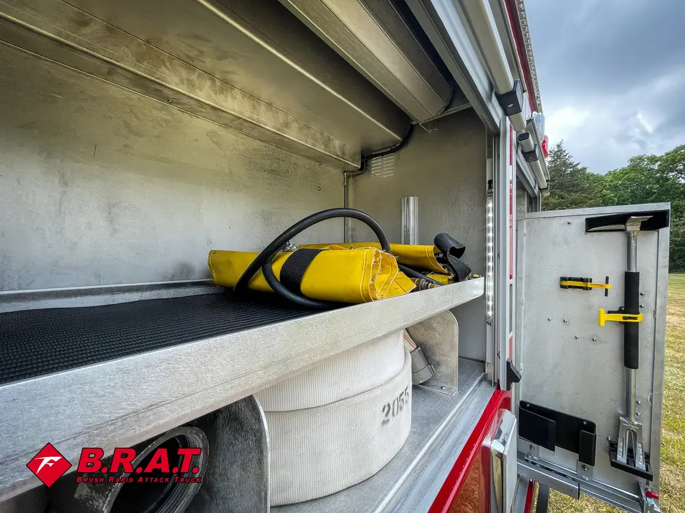 Side compartment close-up with hose roll and yellow portable tool.
