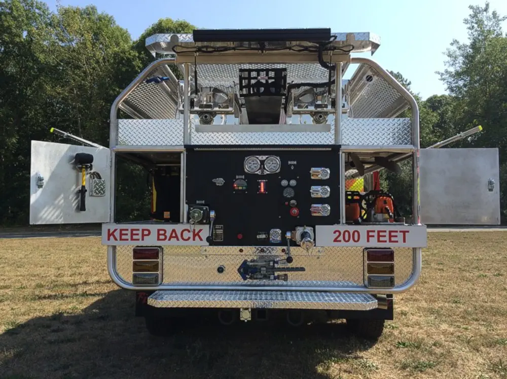 Exterior view of small fire truck showing cab, body compartments, and wheel/tire area.