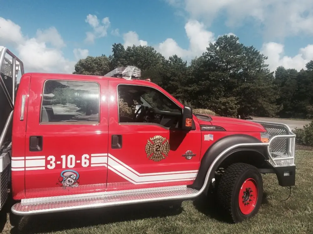Exterior view of small fire truck showing cab, body compartments, and wheel/tire area.