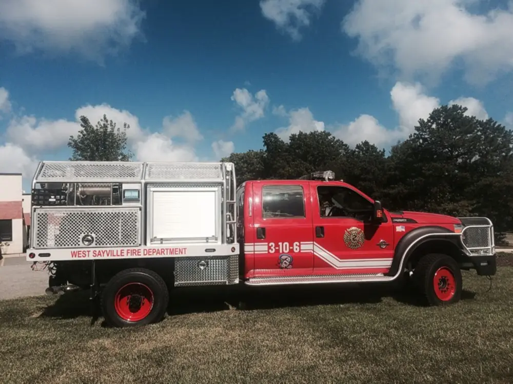 Exterior view of small fire truck showing cab, body compartments, and wheel/tire area.