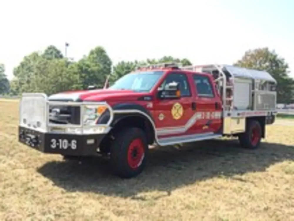 Exterior view of small fire truck showing cab, body compartments, and wheel/tire area.