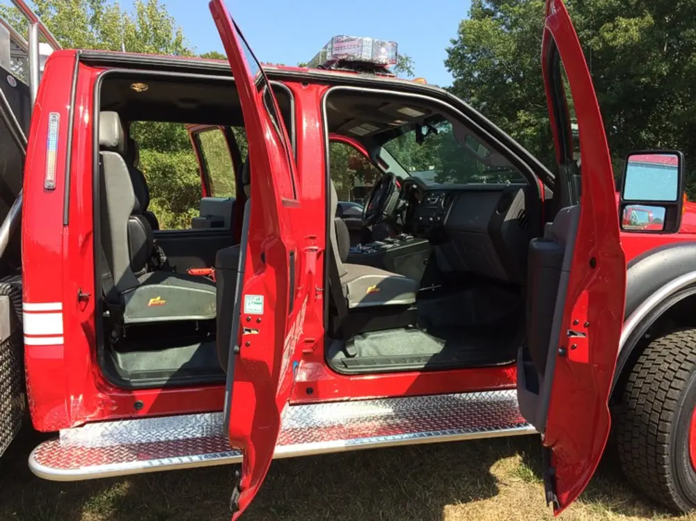 Exterior view of small fire truck showing cab, body compartments, and wheel/tire area.