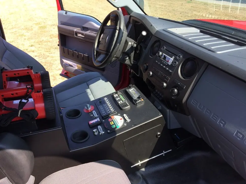 Exterior view of small fire truck showing cab, body compartments, and wheel/tire area.