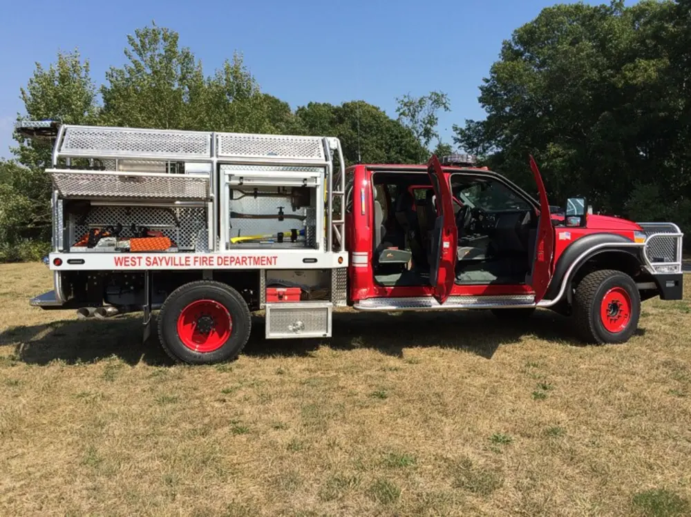 Exterior view of small fire truck showing cab, body compartments, and wheel/tire area.