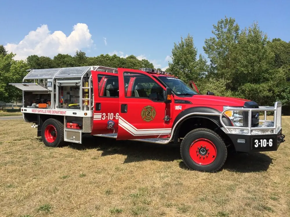 Exterior view of small fire truck showing cab, body compartments, and wheel/tire area.