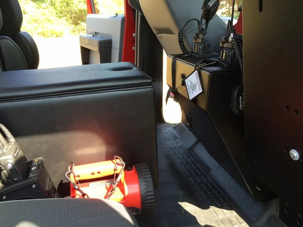 Exterior view of small fire truck showing cab, body compartments, and wheel/tire area.