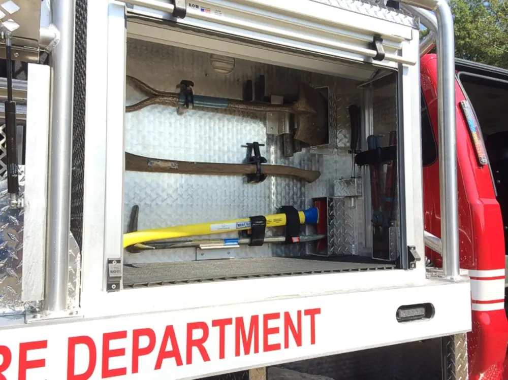 Exterior view of small fire truck showing cab, body compartments, and wheel/tire area.