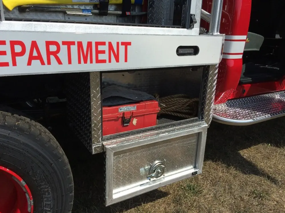 Exterior view of small fire truck showing cab, body compartments, and wheel/tire area.