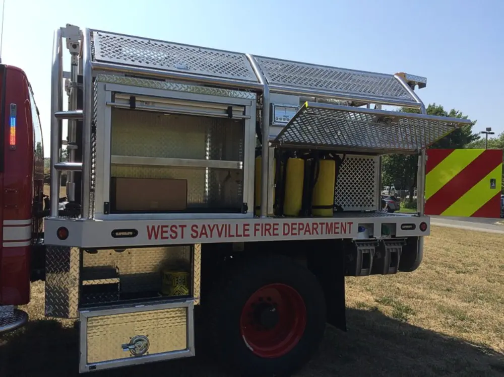 Exterior view of small fire truck showing cab, body compartments, and wheel/tire area.