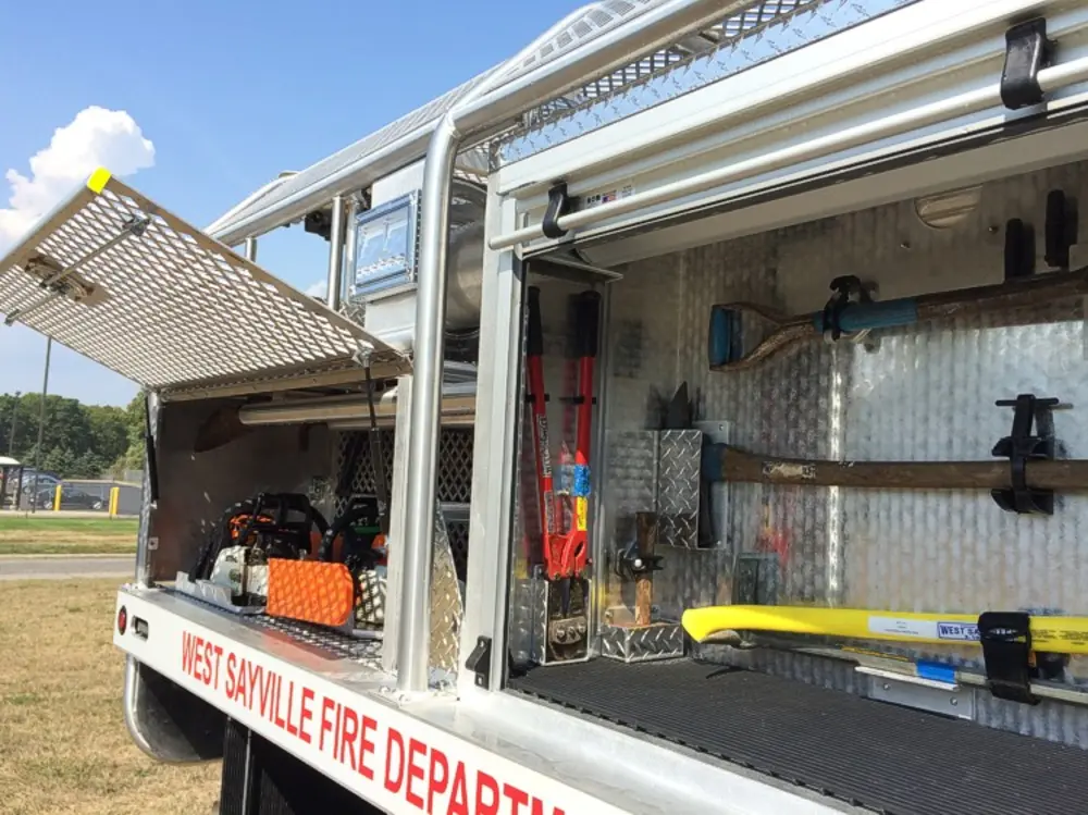Exterior view of small fire truck showing cab, body compartments, and wheel/tire area.