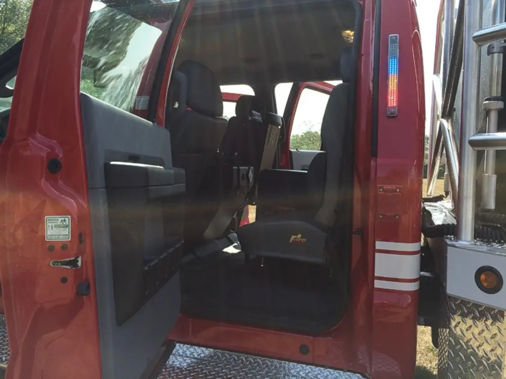Exterior view of small fire truck showing cab, body compartments, and wheel/tire area.