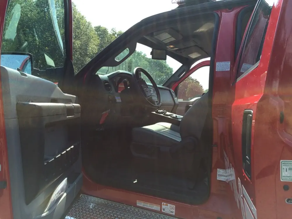 Exterior view of small fire truck showing cab, body compartments, and wheel/tire area.