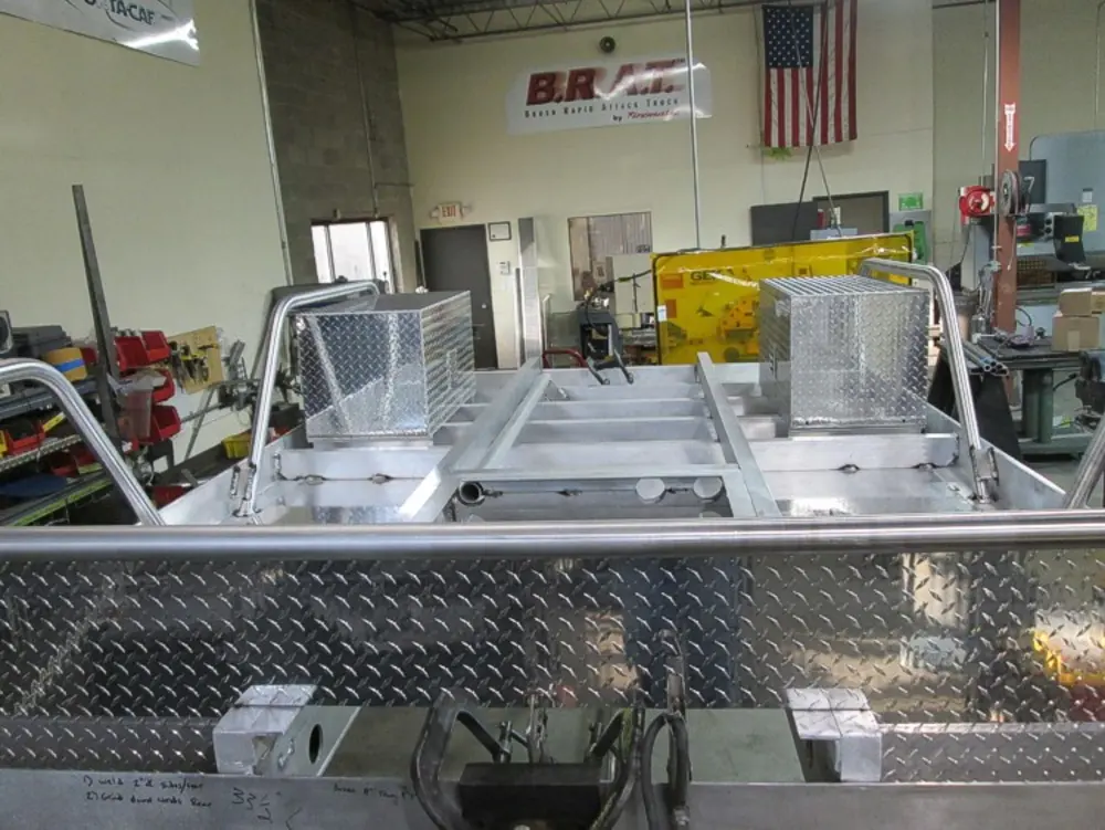 Exterior view of small fire truck showing cab, body compartments, and wheel/tire area.