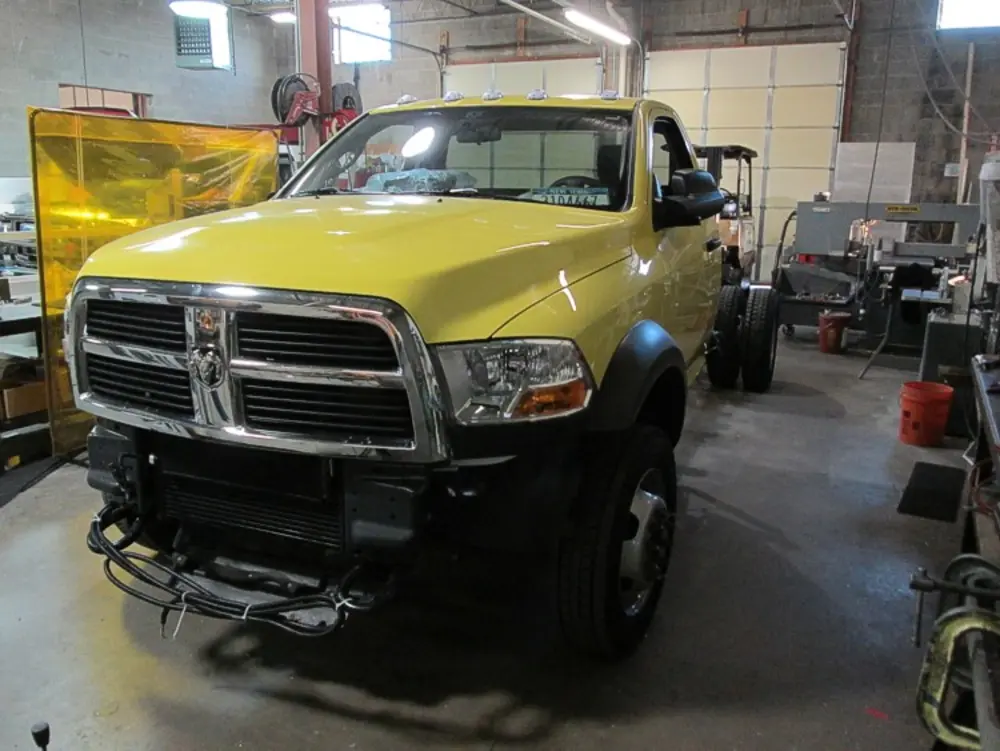 Exterior view of small fire truck showing cab, body compartments, and wheel/tire area.
