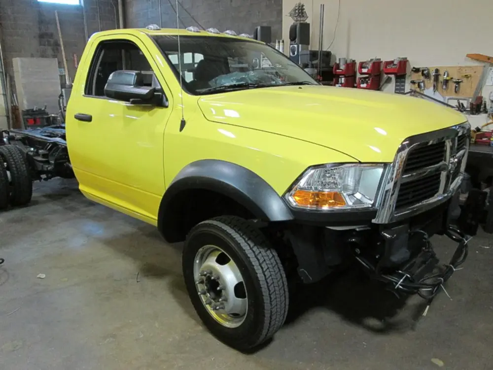 Exterior view of small fire truck showing cab, body compartments, and wheel/tire area.