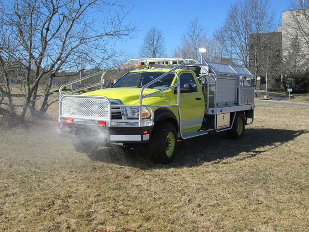 Exterior view of small fire truck showing cab, body compartments, and wheel/tire area.